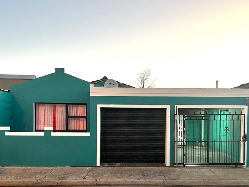 Front facade of a house featuring a teal exterior, a black roller garage door, and a secure metal gate entrance.