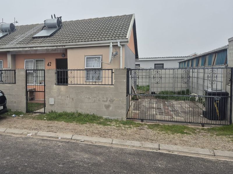 Front exterior view of a single-story semi-detached house featuring a tiled roof, solar water heater, and a gated concrete boundary wall.