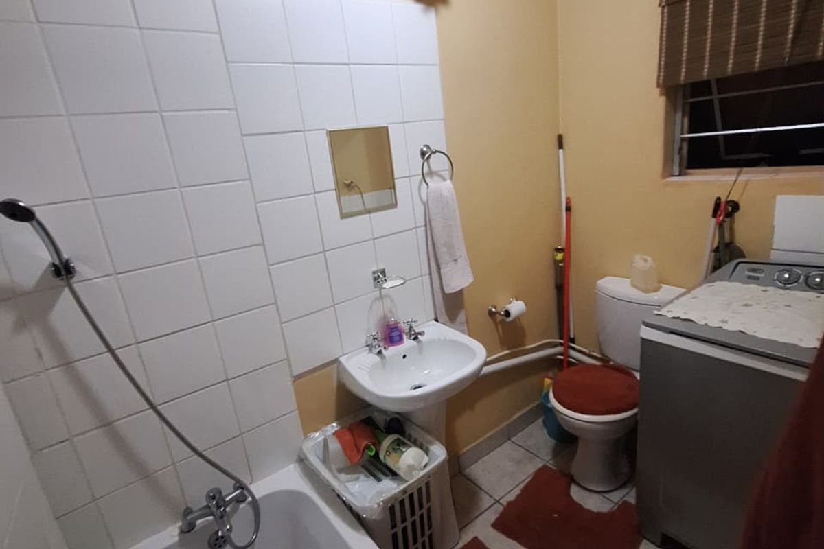 A functional bathroom featuring a bathtub, pedestal basin, and toilet with tiled flooring and splashbacks, offering potential for modernization.