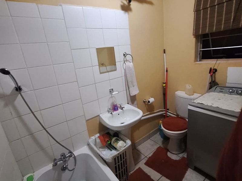 A functional bathroom featuring a bathtub, pedestal basin, and toilet with tiled flooring and splashbacks, offering potential for modernization.