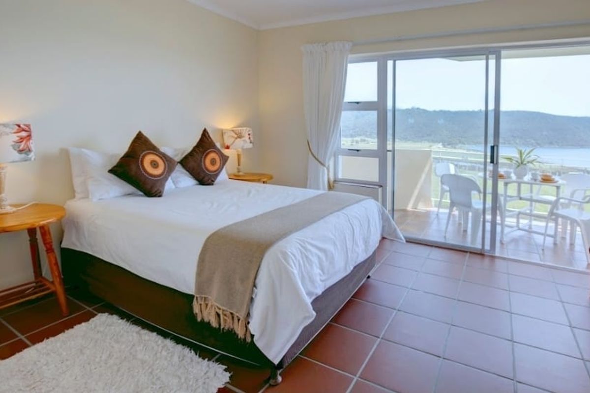 A bright bedroom featuring tiled flooring and large sliding glass doors that open onto a private balcony with scenic coastal views.