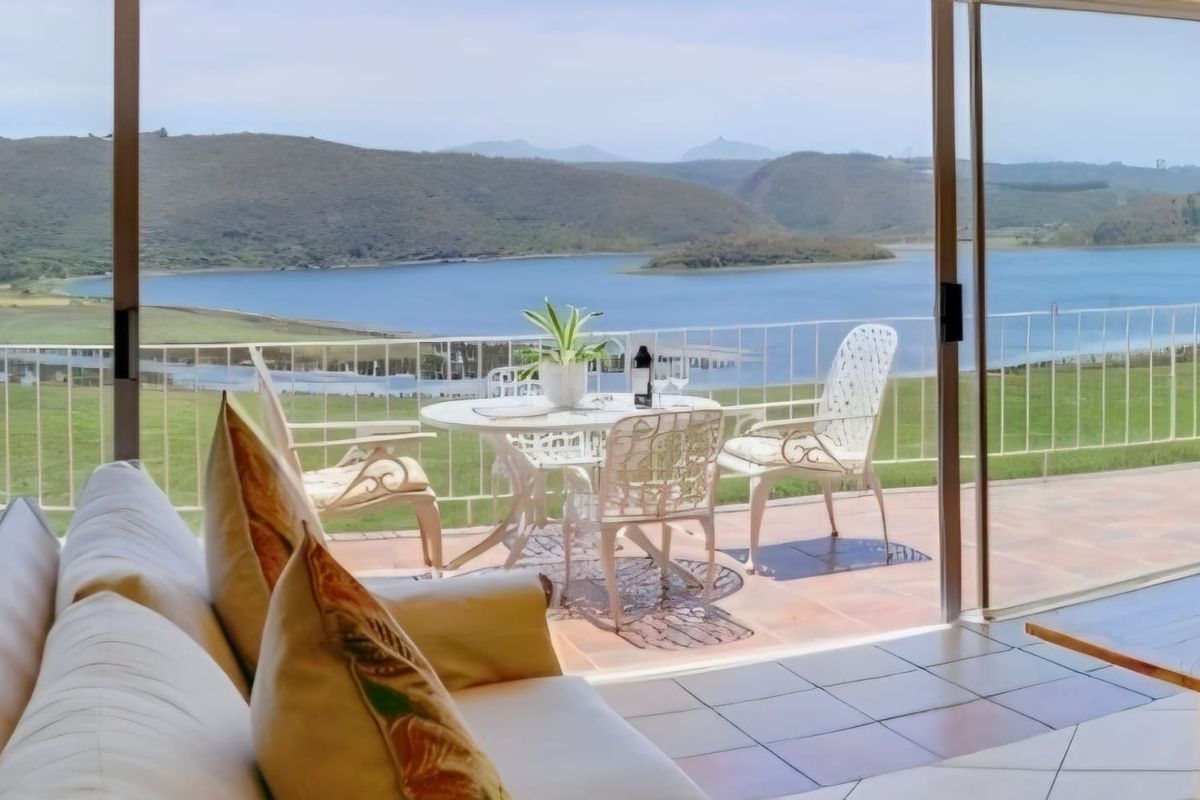 A bright living area featuring large sliding glass doors that open onto a patio with expansive views of the lake and surrounding hills.