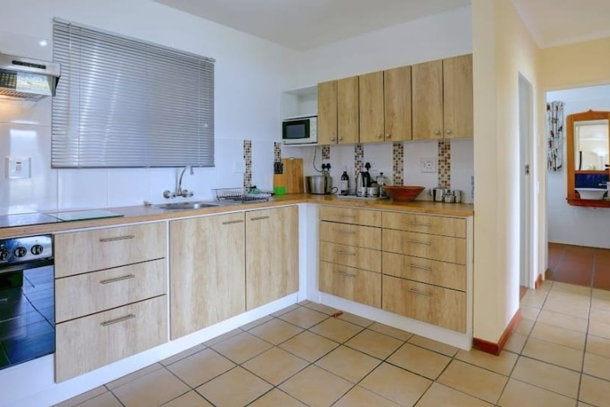 A functional kitchen featuring light wood-look cabinetry, tiled flooring, a built-in oven with extractor fan, and a tiled backsplash.