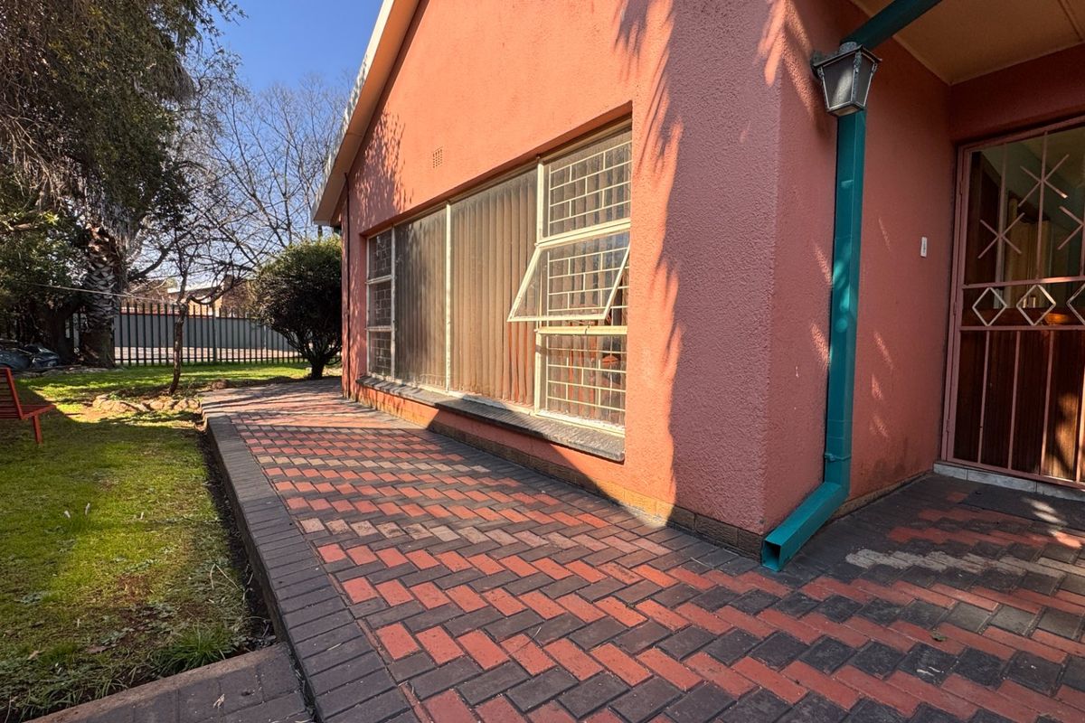 A view of the exterior rear of the house featuring a paved patio area, textured wall finish, and security bars on the windows.