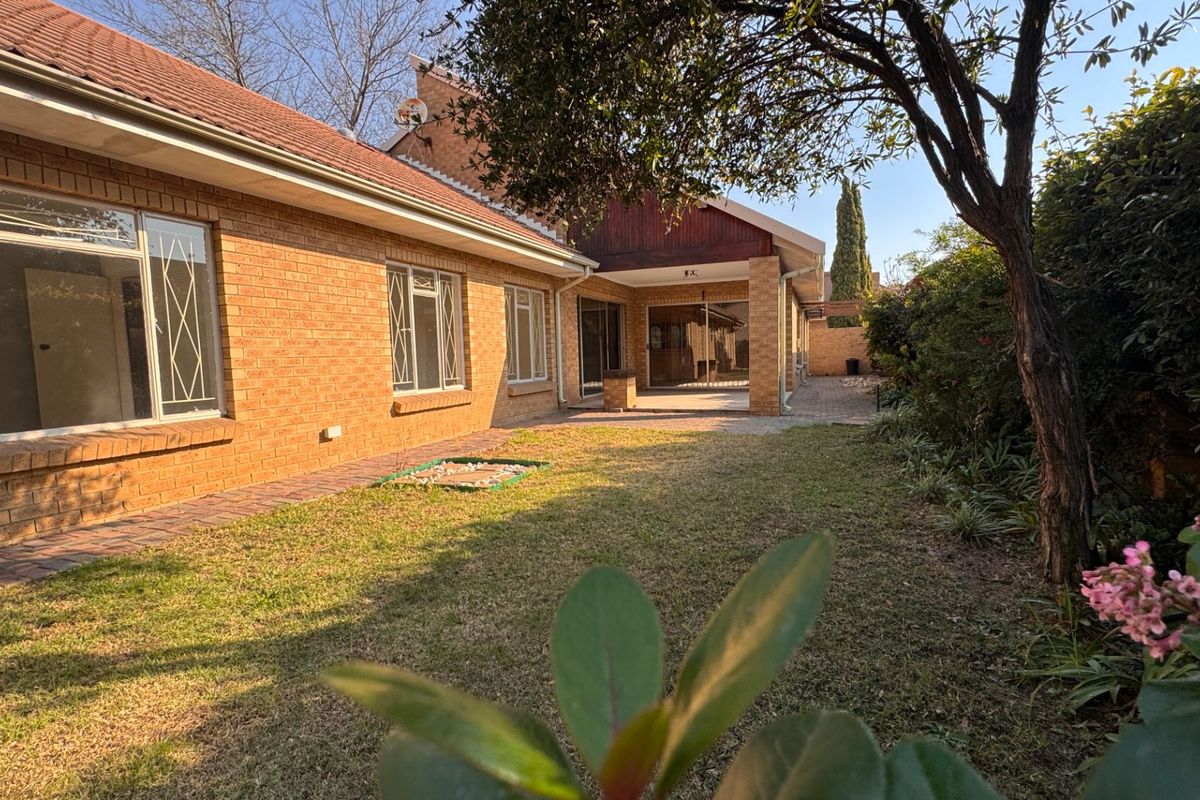 A rear view of the townhouse featuring a brick facade, a covered patio area, and a private garden space.