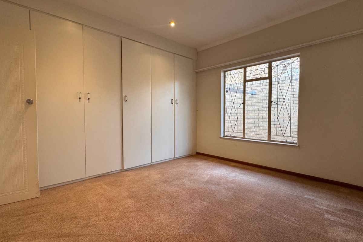 A spacious bedroom featuring extensive built-in cabinetry, neutral carpeting, and a window fitted with security bars.