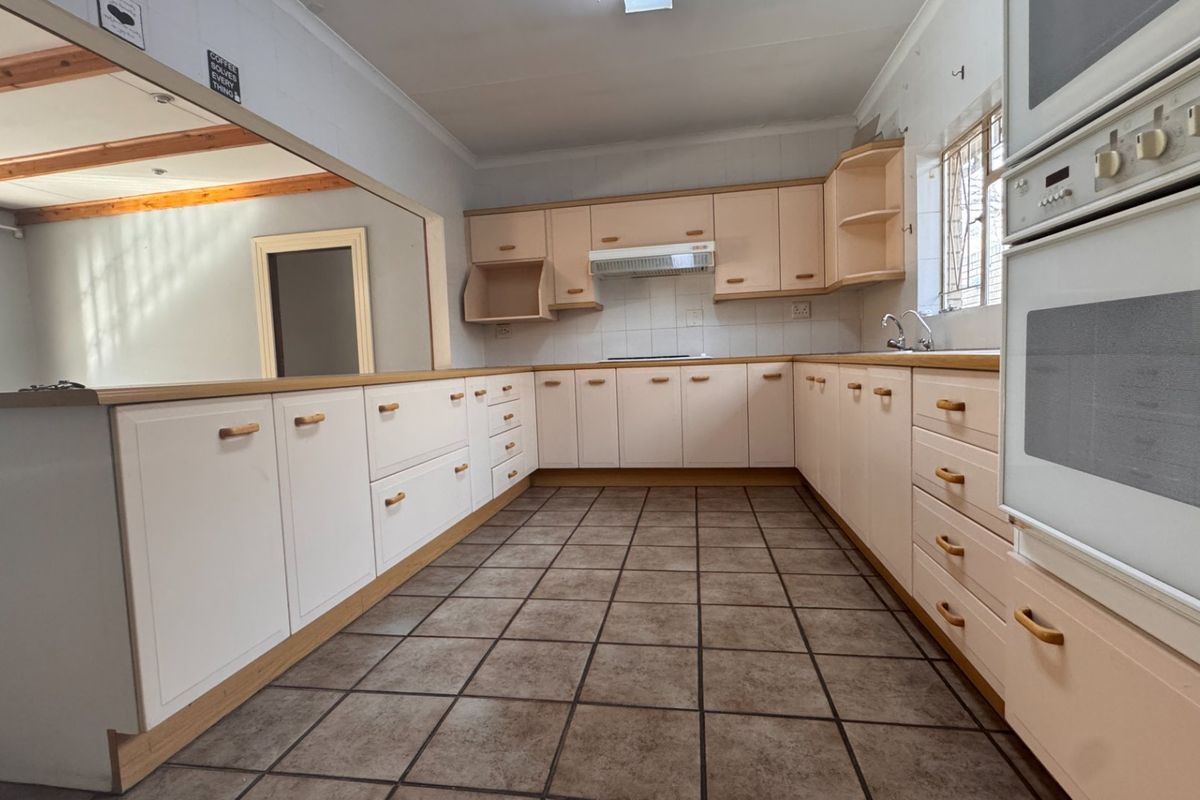 A functional kitchen featuring light-toned cabinetry, built-in oven, extractor fan, and tiled flooring, with an open-plan layout connecting to the adjacent living area.