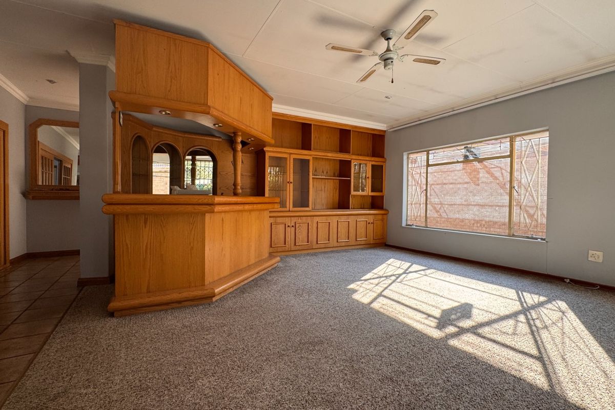 Spacious living area featuring a built-in wooden bar and integrated shelving unit, large window, and ceiling fan.