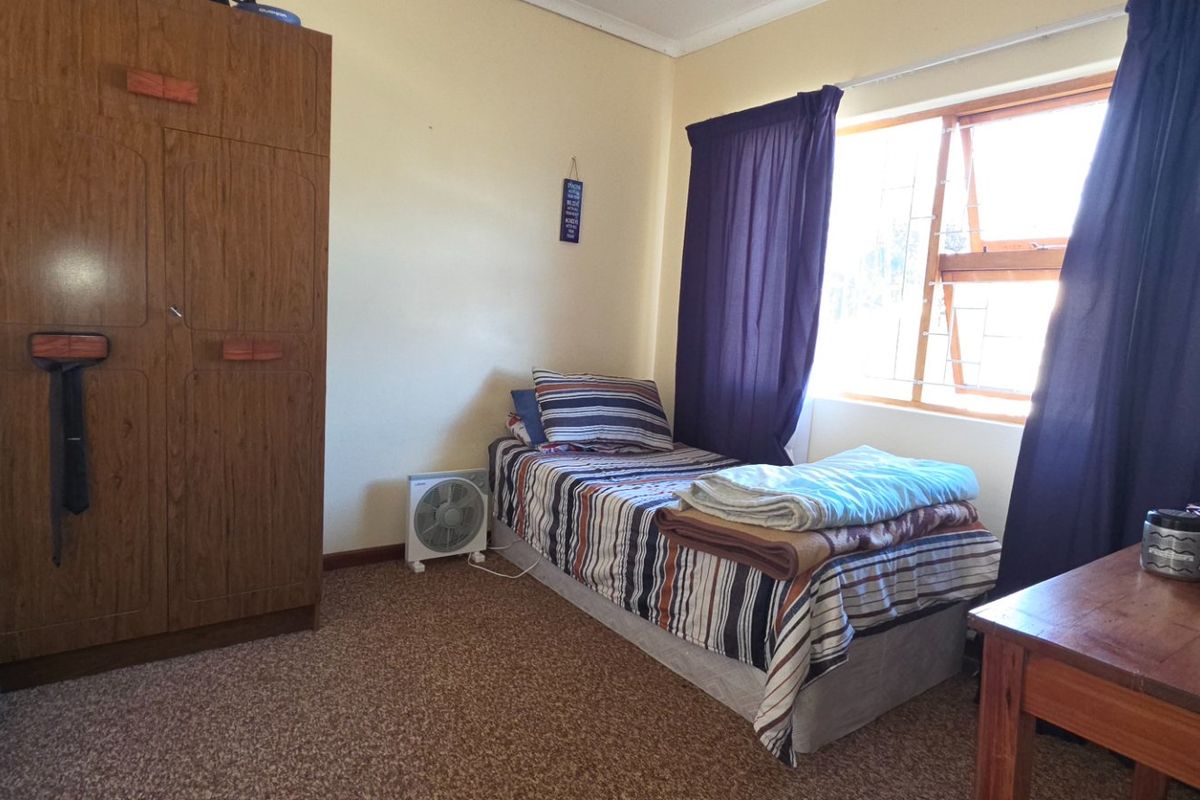 A functional bedroom featuring carpeted flooring, a built-in wardrobe, and a window fitted with security bars.