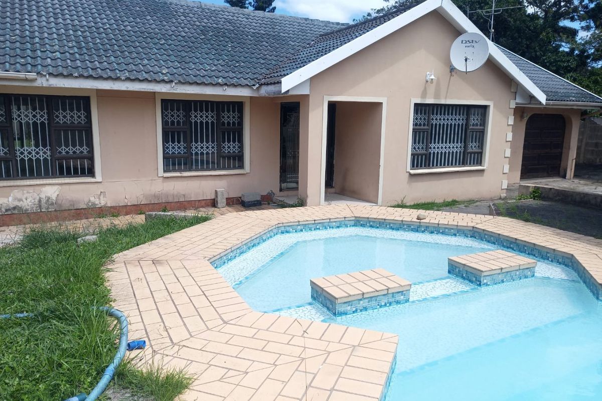 Rear view of the house featuring a swimming pool with tiled surround, security bars on windows, and a tiled roof.