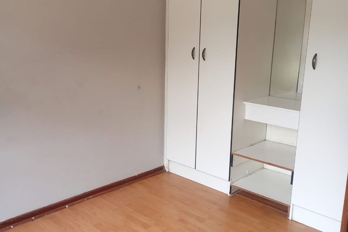 A vacant bedroom featuring laminate flooring, decorative ceiling cornices, and a built-in wardrobe with an integrated vanity mirror and shelving unit.