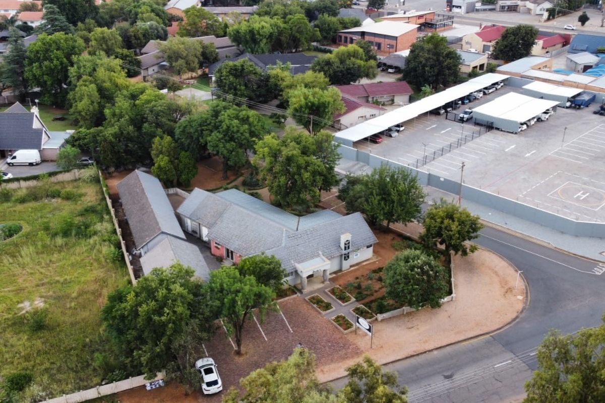 Aerial view of the commercial property featuring a tiled roof building, landscaped garden, paved parking area, and adjacent covered parking facilities.