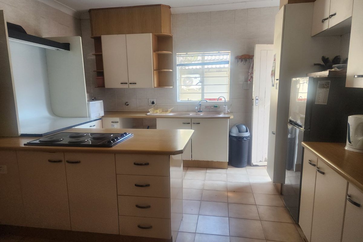 A functional kitchen featuring built-in cabinetry, laminate countertops, an integrated electric hob, and tiled flooring with a rear access door.