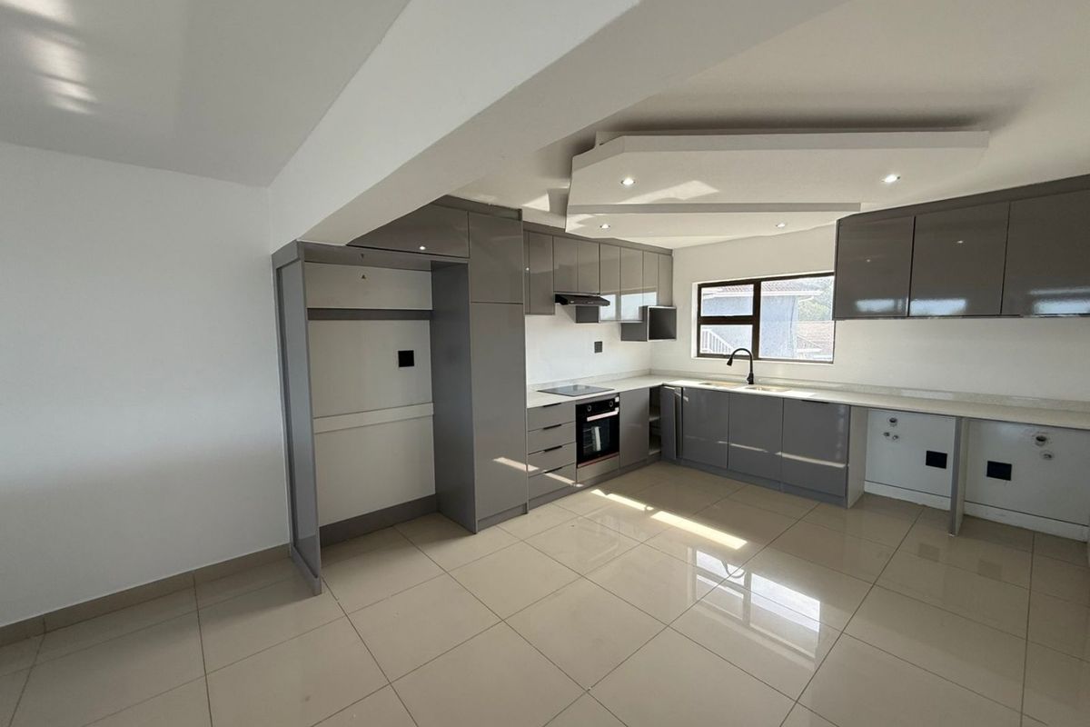 Modern kitchen featuring sleek grey cabinetry, stone countertops, integrated appliances, and recessed ceiling lighting in a bright, open-plan space.