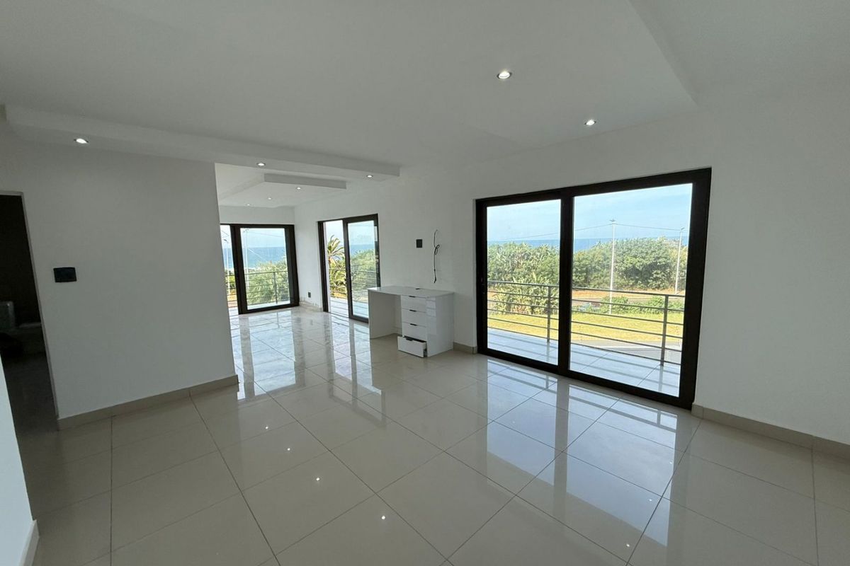Spacious, modern open-plan living area featuring polished porcelain tiles, recessed lighting, and large sliding glass doors opening to a scenic balcony with ocean views.