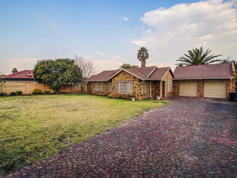 Front view of a brick house featuring a large lawn, paved driveway, and a double garage with roller doors.