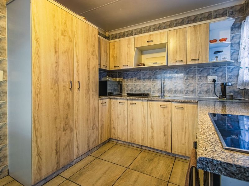 A functional kitchen featuring light wood-look cabinetry, granite-style countertops, tiled backsplash, and ceramic floor tiles with a built-in hob.