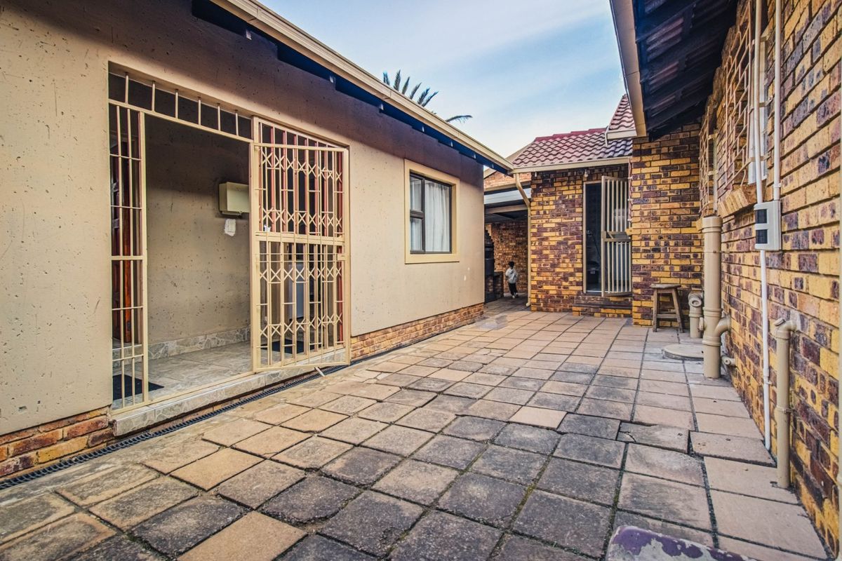 A paved rear courtyard area featuring brick and plastered wall finishes with secure metal gates providing access to the property.