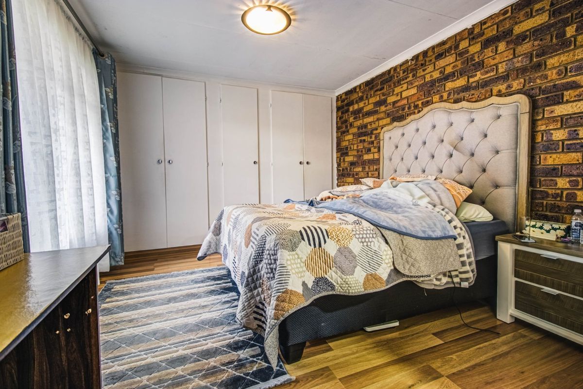 A bedroom featuring an exposed brick feature wall, laminate flooring, and ample built-in cupboard storage.