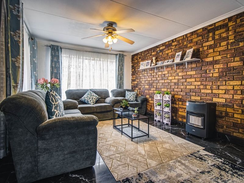 A cozy living room featuring an exposed brick feature wall, dark tiled flooring, and a ceiling fan, creating a warm and inviting atmosphere.
