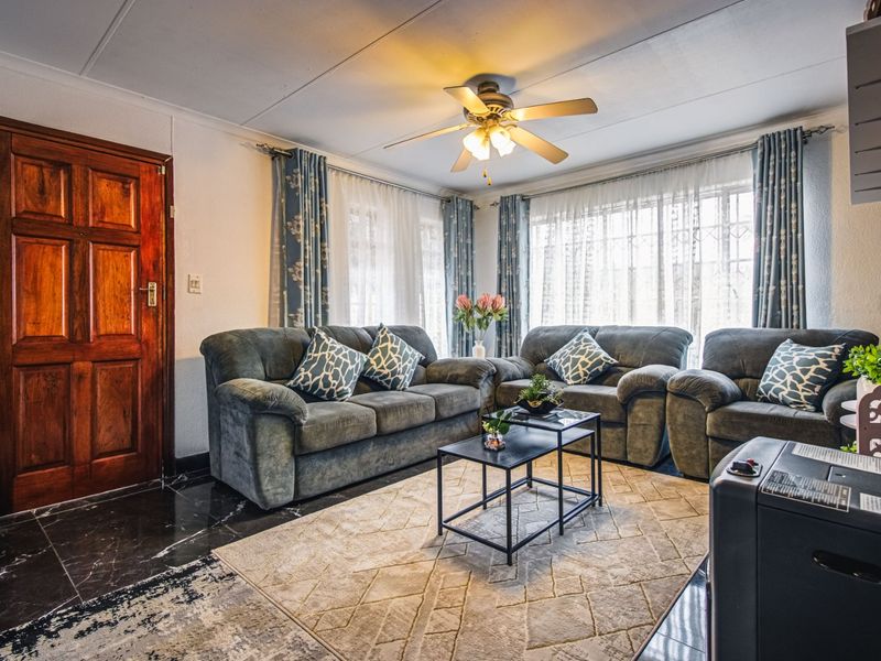 A comfortable living room featuring dark tiled flooring, an exposed brick accent wall, and a central ceiling fan, providing a cozy and functional space.