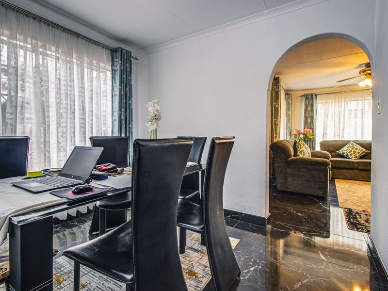 Open-plan dining and living area featuring elegant marble-look floor tiles, an arched transition, and a ceiling fan, creating a connected and functional living space.
