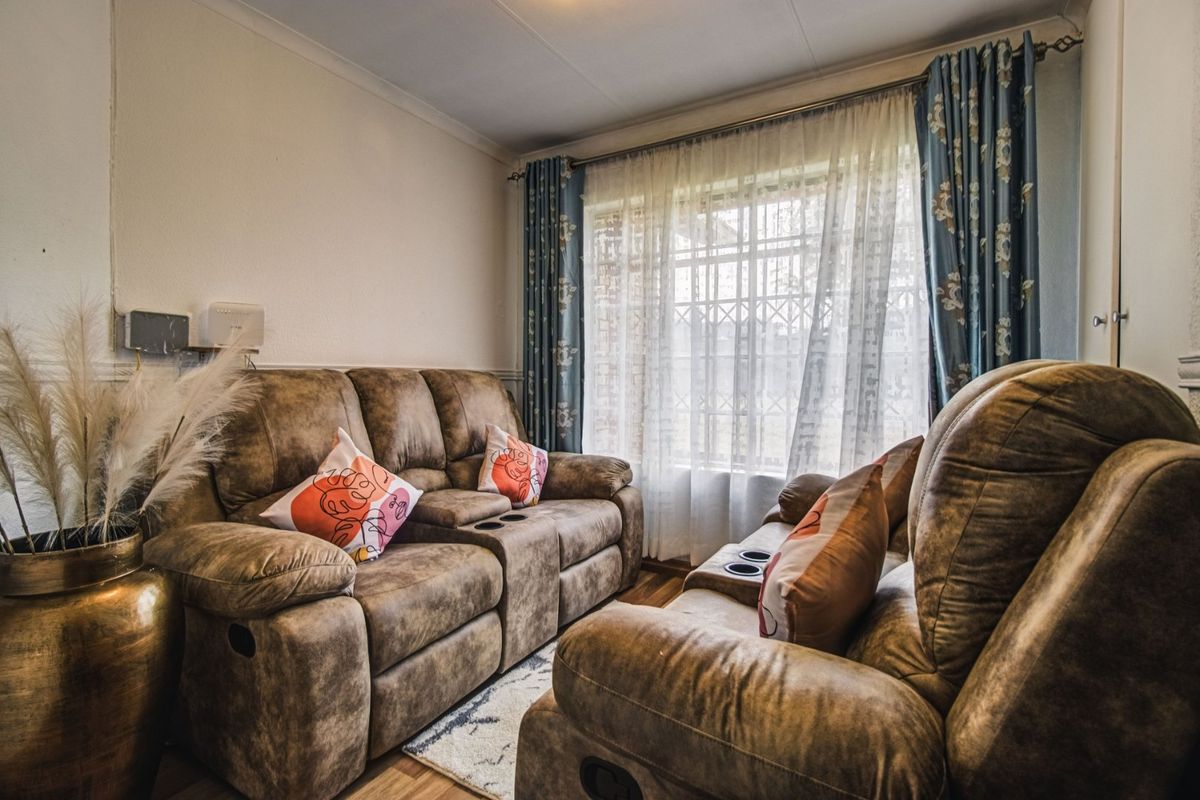 A cozy living room featuring laminate flooring, coving, and a window fitted with a security gate.