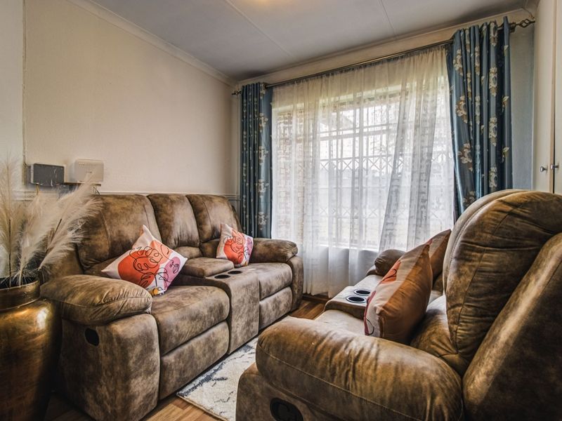 A cozy living room featuring laminate flooring, coving, and a window fitted with a security gate.