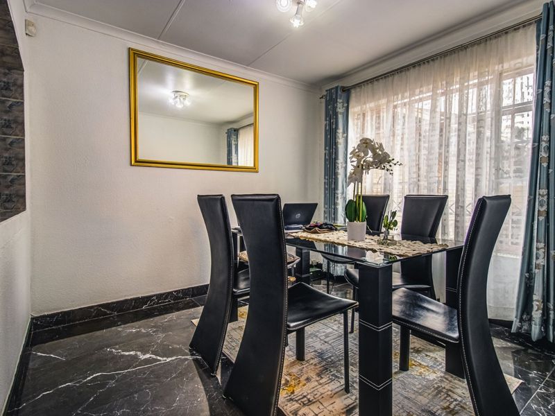 A well-maintained dining room featuring polished marble-look floor tiles, coved ceilings, and large windows with curtain treatments.