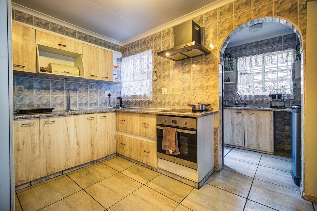 A functional kitchen featuring light wood-look cabinetry, tiled backsplash, built-in oven and hob, and an adjoining scullery area with additional sink and storage.