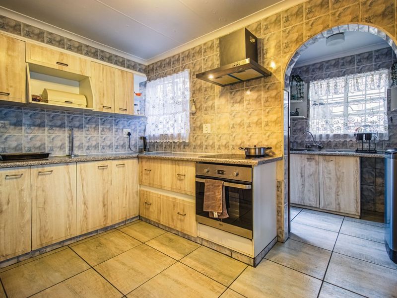 A functional kitchen featuring light wood-look cabinetry, tiled backsplash, built-in oven and hob, and an adjoining scullery area with additional sink and storage.