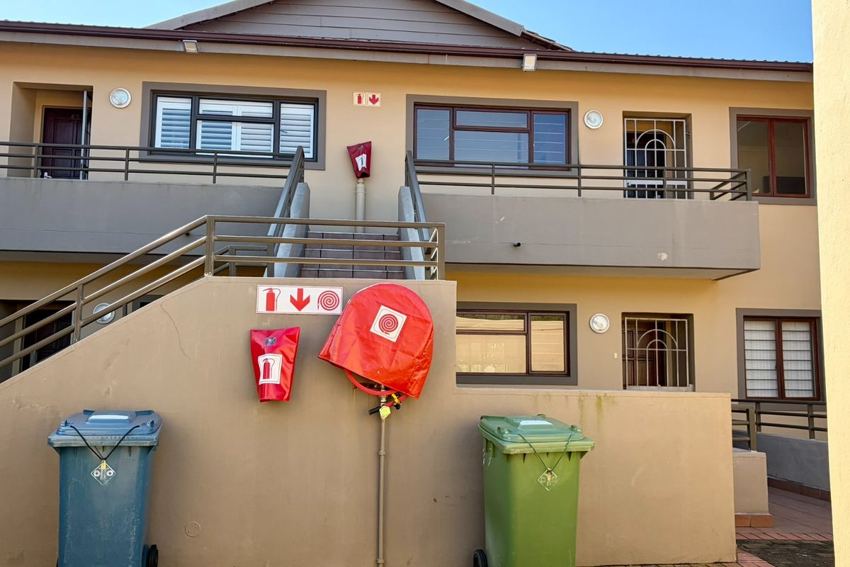 Exterior view of an apartment complex featuring a metal staircase, security bars on windows, and essential fire safety equipment installed on the building facade.