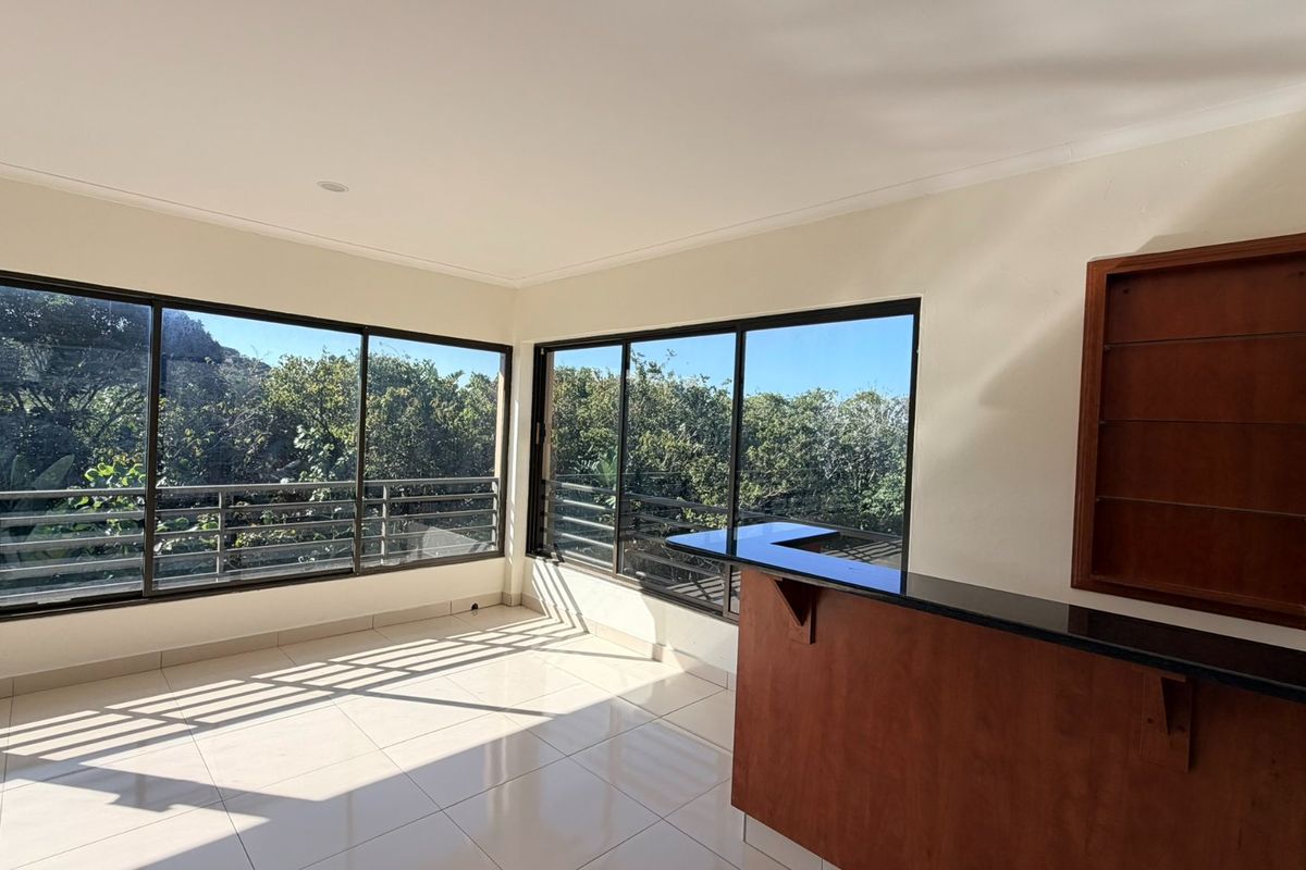 Bright and spacious living area featuring large windows with natural light, tiled flooring, and a built-in bar counter with shelving.