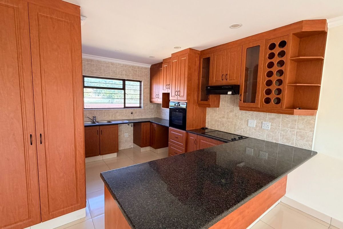 A well-maintained kitchen featuring warm-toned wooden cabinetry, granite countertops, built-in oven, electric hob, and a functional layout with ample storage space.