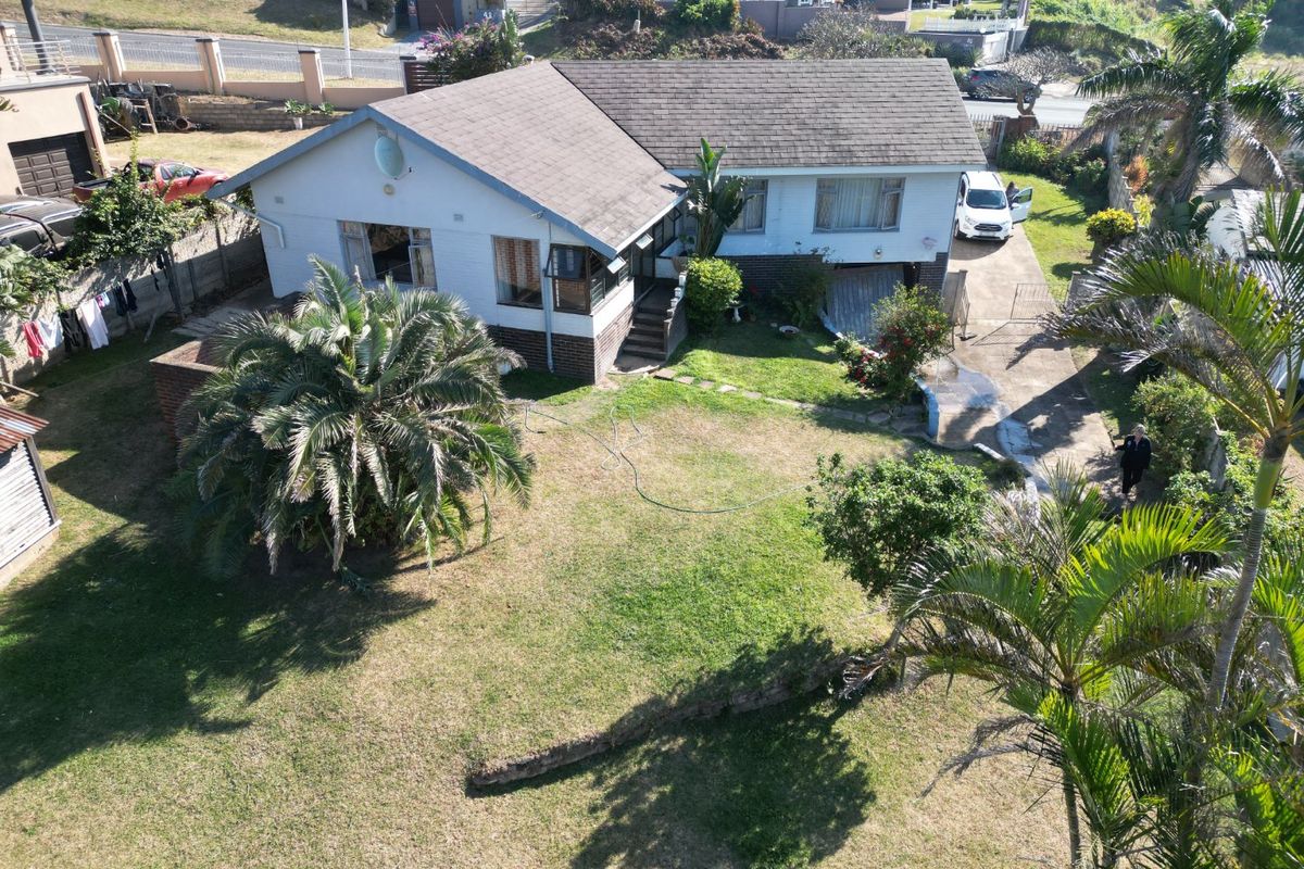 Aerial view of a residential property featuring a single-story house with a tiled roof, surrounding garden, and concrete driveway.