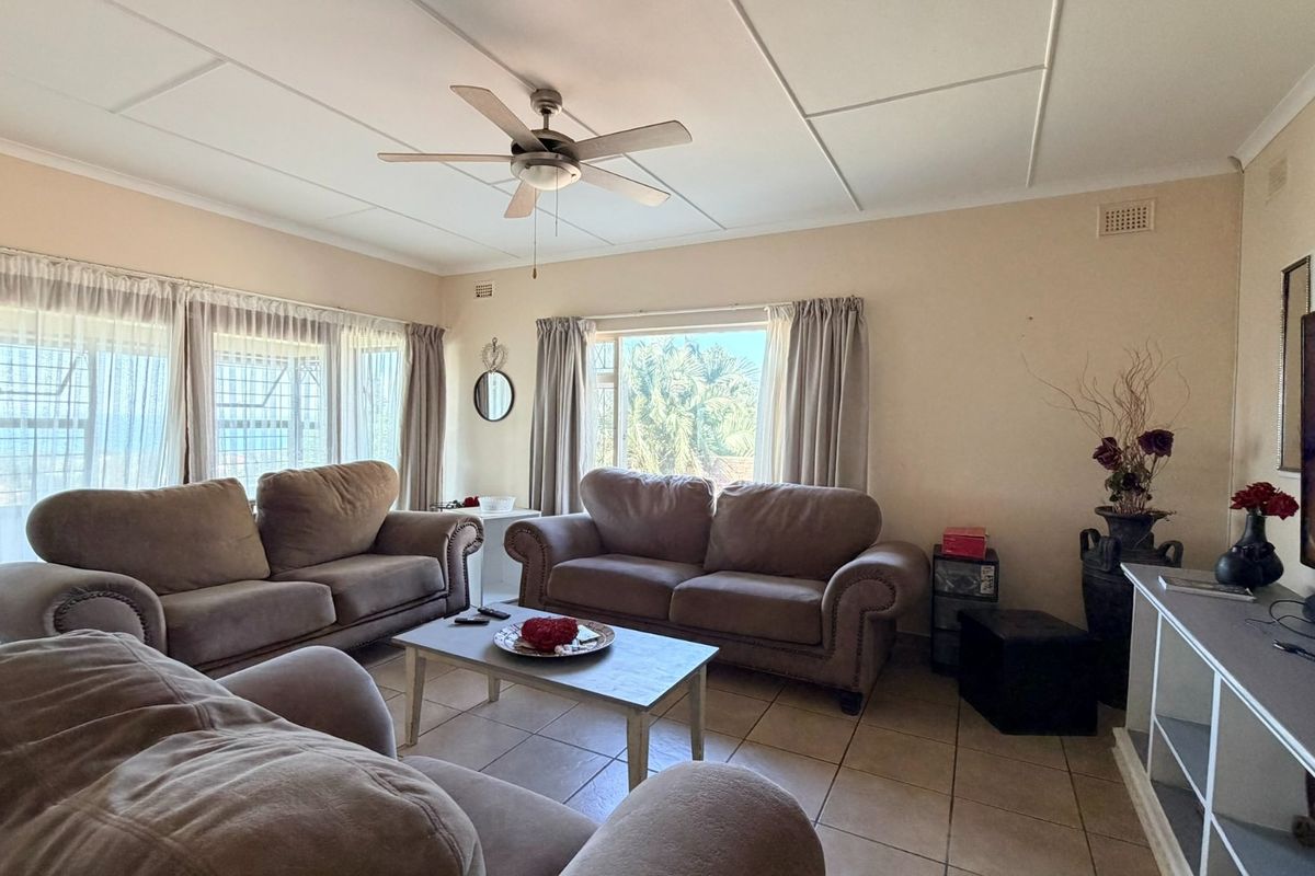 A comfortable living room featuring tiled flooring, a ceiling fan, and large windows that provide ample natural light.