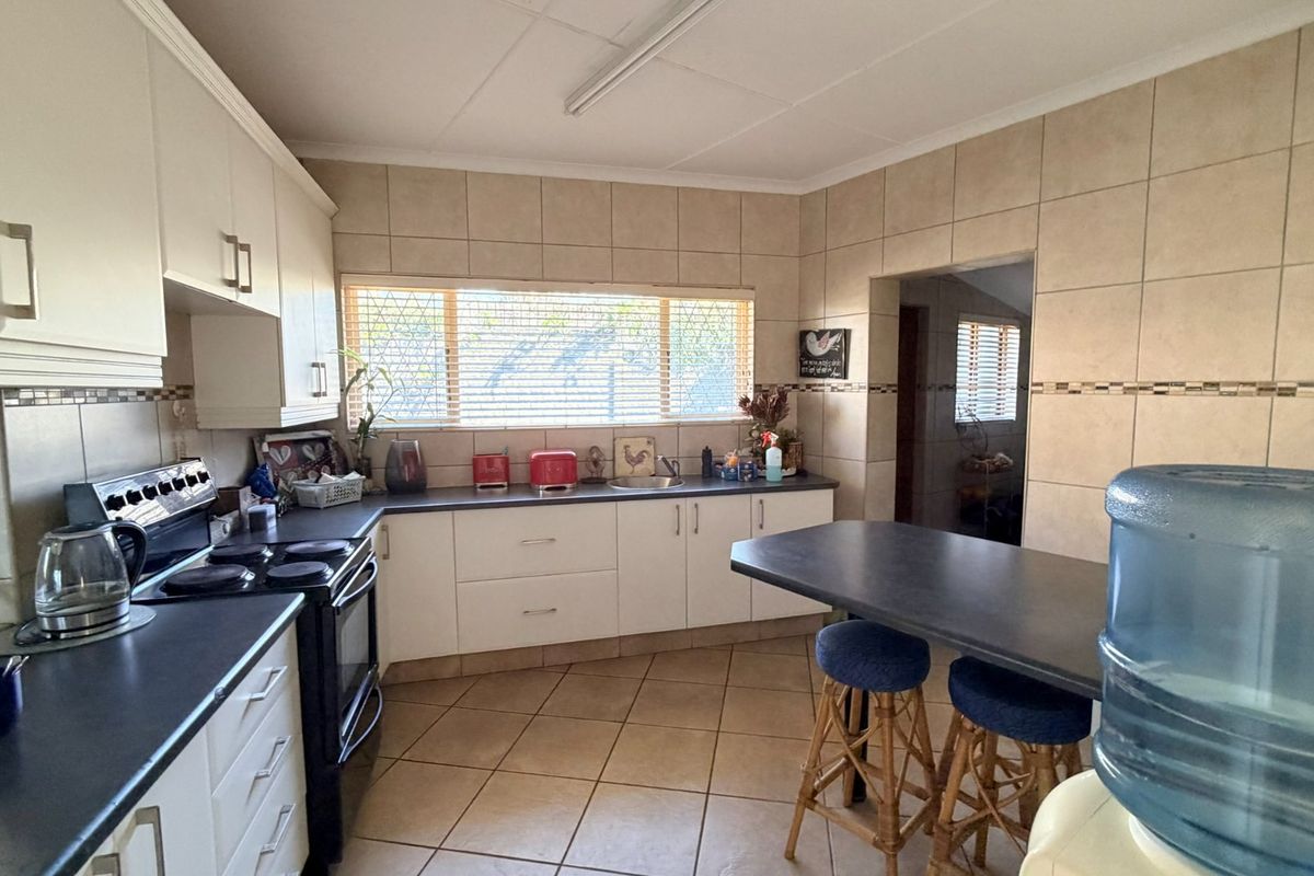 Functional kitchen featuring white cabinetry, dark countertops, tiled backsplash, and a breakfast bar area with direct access to an adjacent room.