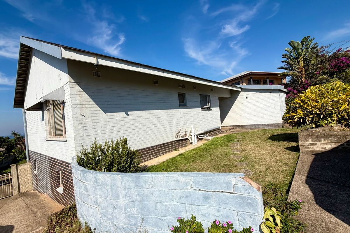 Rear view of the property showing a brick exterior, concrete driveway, and a garden area with a retaining wall.