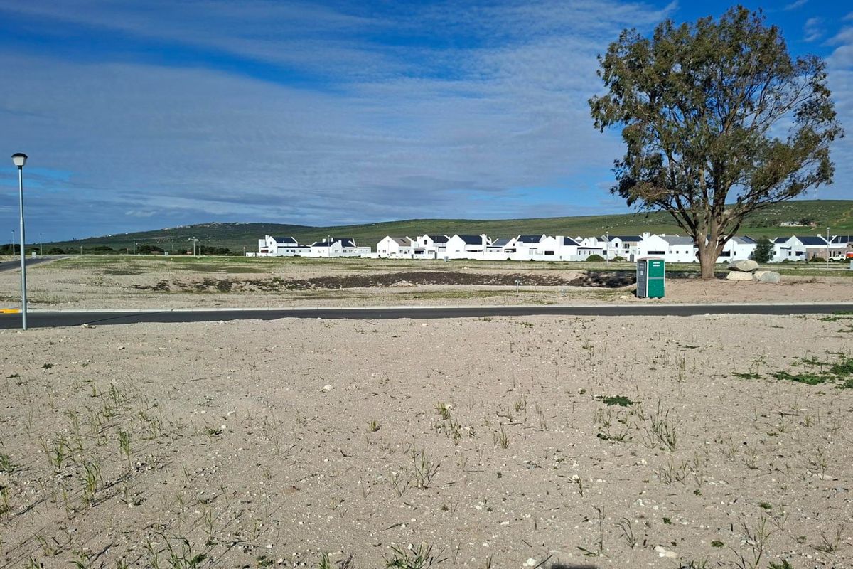 A view of a vacant residential plot featuring paved road access and street lighting, situated within a developed estate.