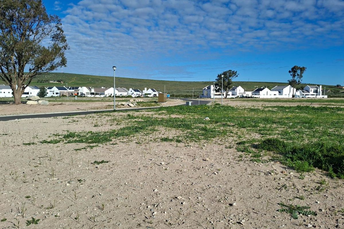 A view of a vacant residential plot featuring paved road access and street lighting, situated within a developed estate.