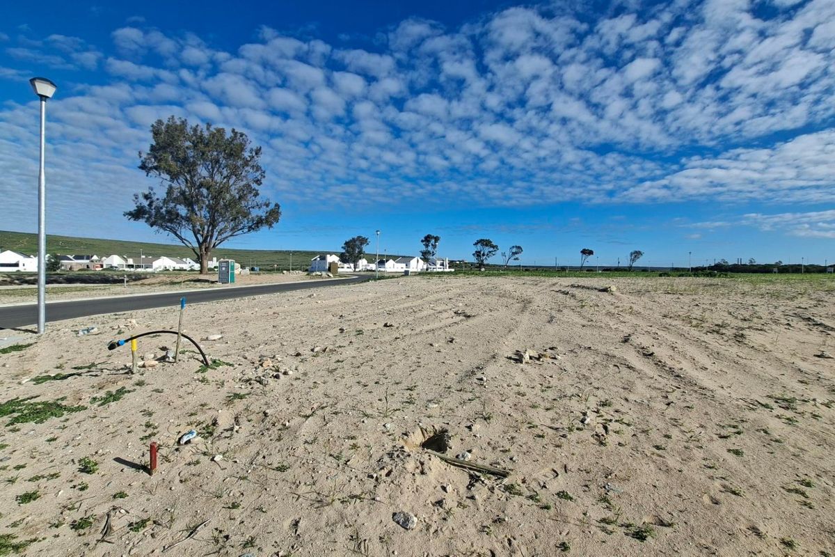 A vacant residential plot featuring level sandy terrain, street lighting, and visible utility connection points, situated within a developed residential estate.