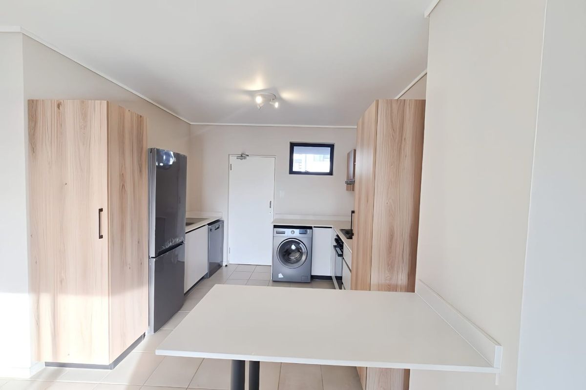 Modern kitchen featuring light wood-finish cabinetry, tiled flooring, a breakfast counter, and integrated appliances including a hob, oven, and extractor fan.