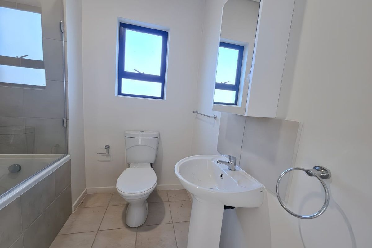 A clean, modern bathroom featuring a pedestal basin, toilet, and a bathtub with a glass shower screen, finished with neutral floor tiles.