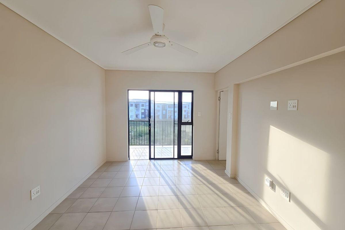 An empty, well-lit living room featuring neutral tiled flooring, a ceiling fan, and sliding glass doors providing access to a balcony.