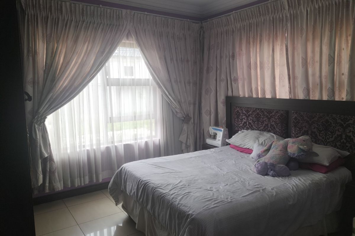A bedroom featuring tiled flooring, decorative cornicing, and large windows with layered curtains, providing a functional and well-lit living space.
