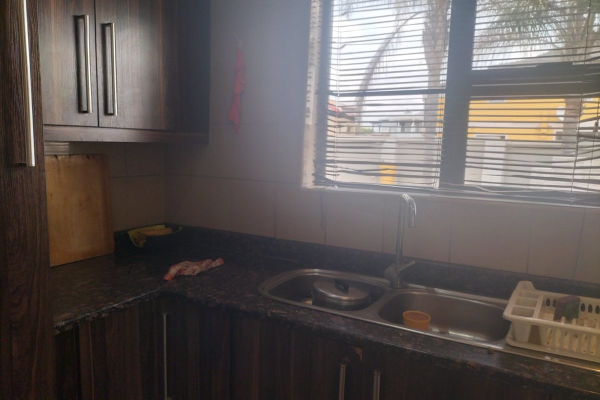A functional kitchen area featuring dark wood cabinetry, granite countertops, and a double bowl stainless steel sink with a window view.