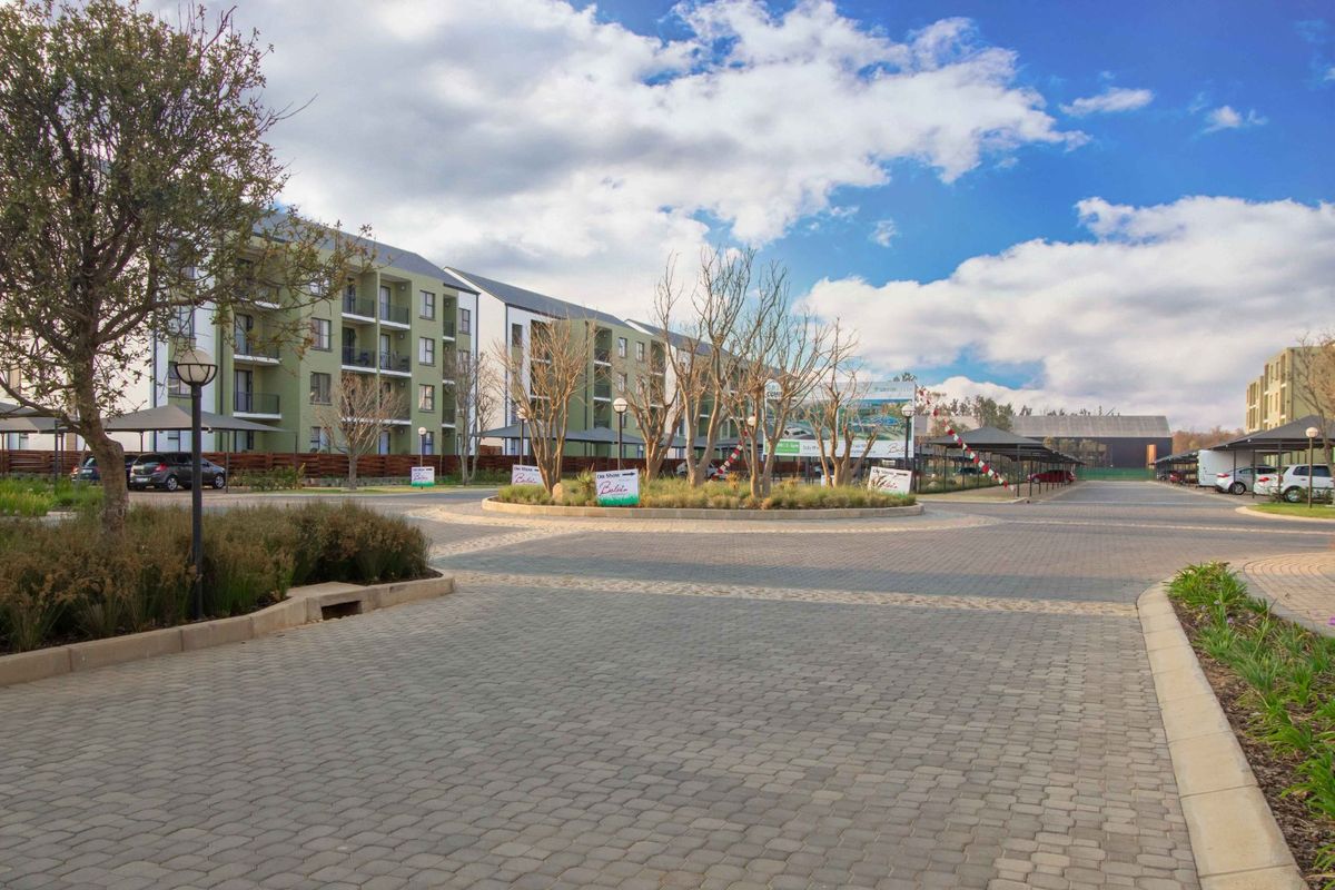 A view of the apartment complex entrance featuring a paved driveway, landscaped roundabout, and covered parking facilities within a well-maintained residential estate.