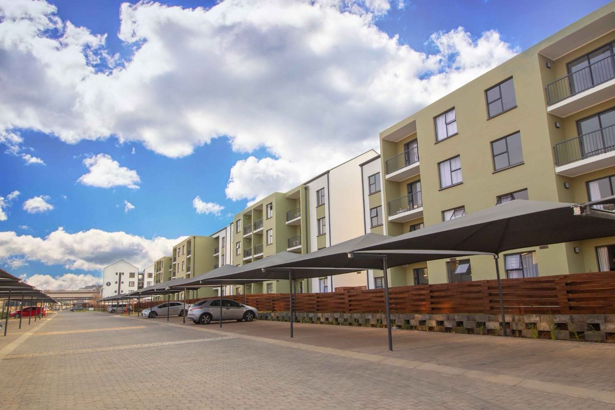 Exterior view of a modern apartment complex featuring paved parking areas with shade cloth carports and multi-story residential units with balconies.