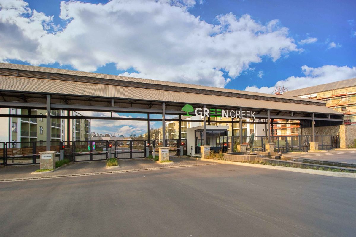 The main entrance gate and security checkpoint for the Greencreek apartment complex, featuring a modern metal structure and landscaped water feature.