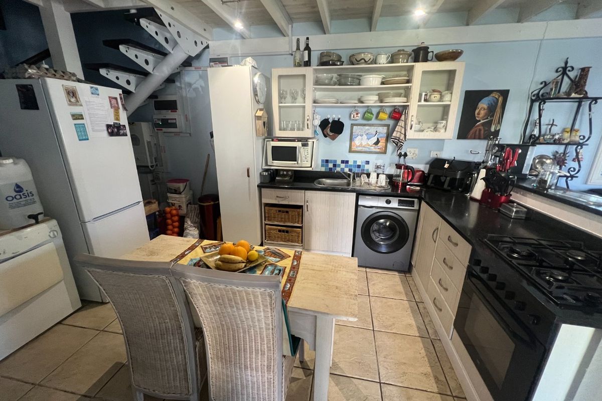 Functional kitchen featuring built-in cabinetry, integrated oven, gas hob, and tiled flooring, with an adjacent staircase and exposed beam ceiling.